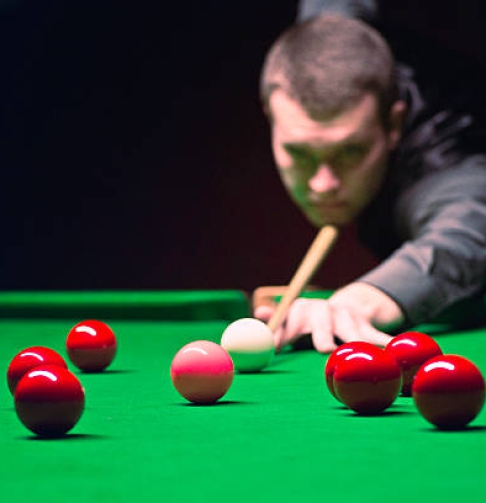 Snooker player going for pink. Ball in focus, face blurred in distance. Ambient light, slightly toned for atmosphere